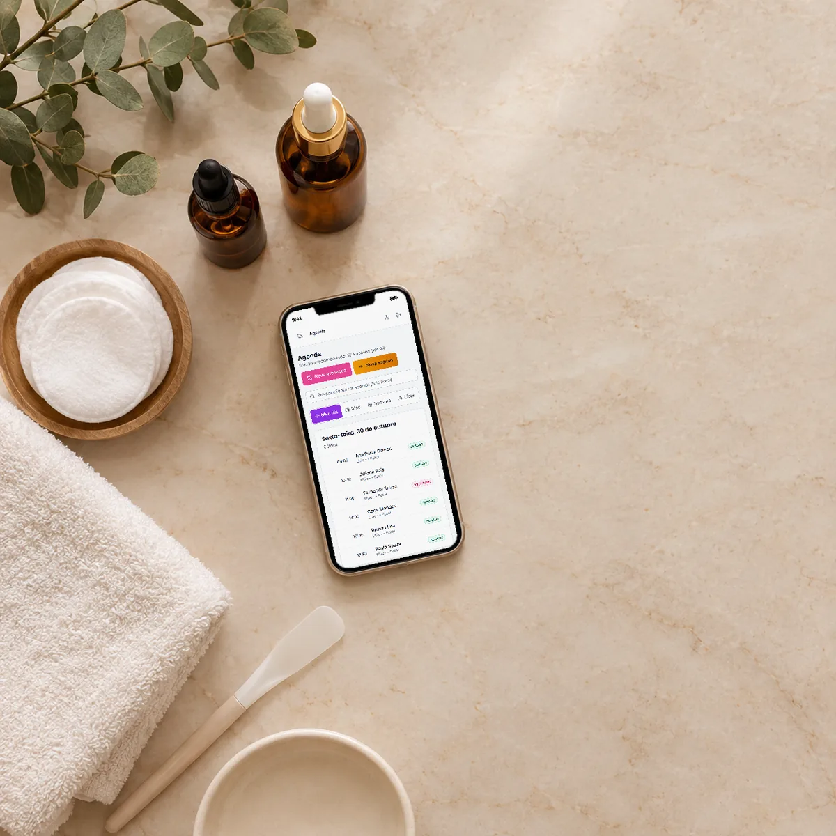 Celular sobre a bancada de estética, com a agenda do dia do GlowBoard aberta, ao lado de séruns, algodão e toalha